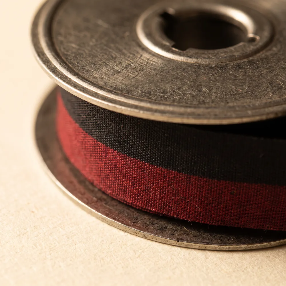A two-colour typewriter ribbon on a metal twin spool, black above and red below.